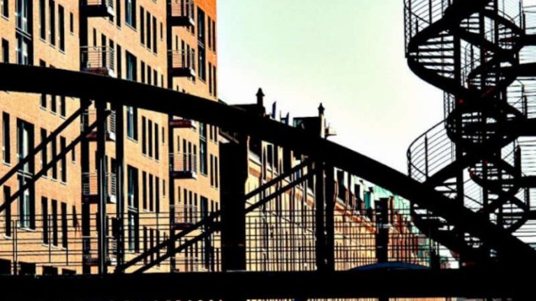 Brücke Ein rötliches Backstein-Gebäude, davor eine Brücke und daneben eine Wendeltreppe