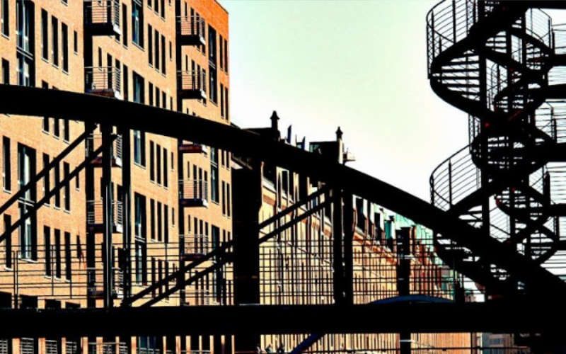 Ein rötliches Backstein-Gebäude, davor eine Brücke und daneben eine Wendeltreppe