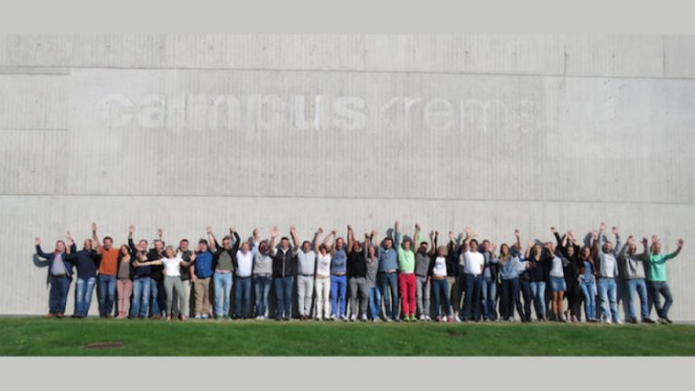 Chiropraktik Campus Eine große Gruppe von Personen steht vor einem Campus Gebäude, alle winken