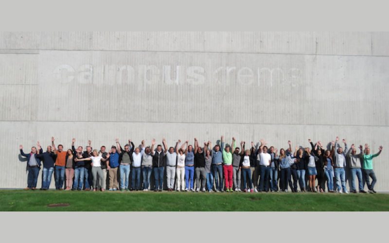Chiropraktik Campus Eine große Gruppe von Personen steht vor einem Campus Gebäude, alle winken