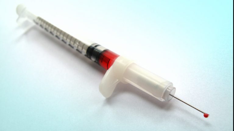 Spritze Aufgezogene Spritze in der sich eine rote durchscheinende Flüssigkeit befindet und ein Tropfen aus der Nadel fließt