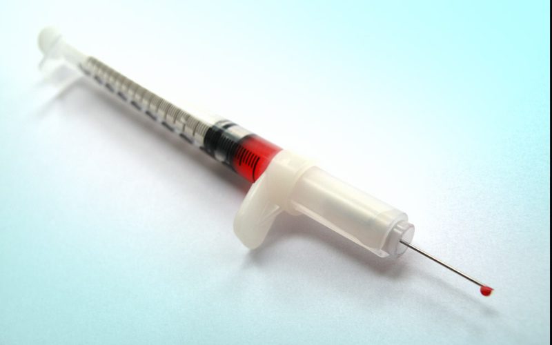 Spritze Aufgezogene Spritze in der sich eine rote durchscheinende Flüssigkeit befindet und ein Tropfen aus der Nadel fließt