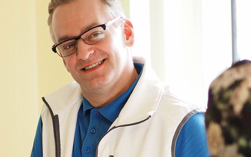 Ralf Kaufmann Ein grinsender Mann mit Brille und einer weißen Weste und blauem Shirt