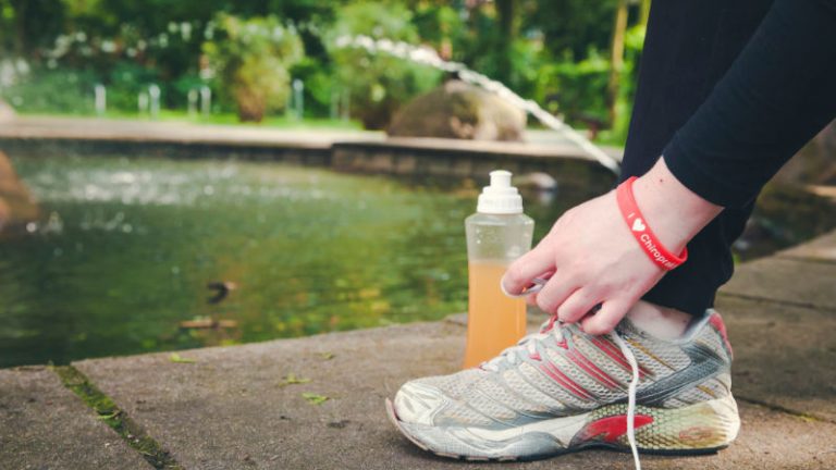 An einem Teich bindet jemand einen Schuh, daneben steht eine Trinkflasche mit orangem Getränk