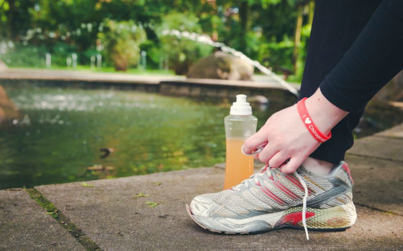 Sport An einem Teich bindet jemand einen Schuh, daneben steht eine Trinkflasche mit orangem Getränk