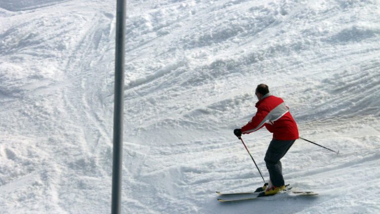Ein Skifahrer mit einer roten Jacke, fährt einen von Schnee bedeckten Berg hinab.
