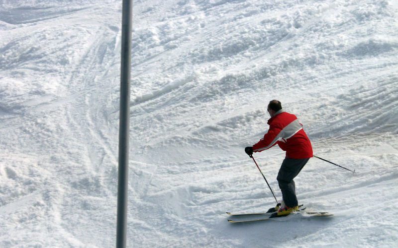 Ein Skifahrer mit einer roten Jacke, fährt einen von Schnee bedeckten Berg hinab.
