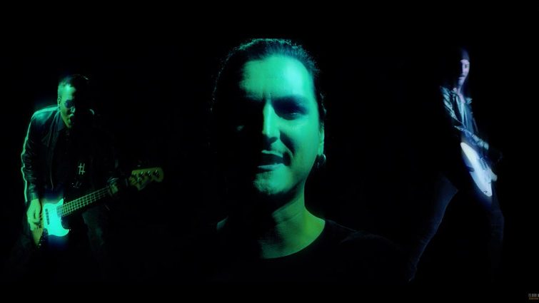 Eine Filmszene aus dem Musikvideo des Musikers Florian Grey, zu sehen sind auf schwarzem Hintergrund 3 Männer, davon einer mit Gitarre links, in der Mitte ein Kopf und rechts ein weiterer Gitarrenspieler.