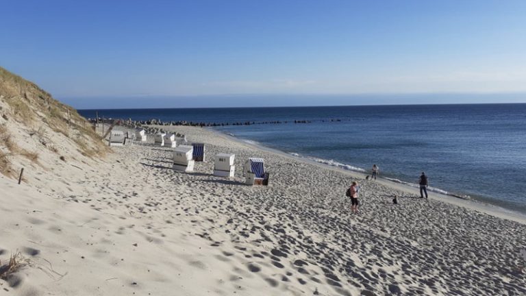Ein Strandpanorama auf der Insel Sylt mit einigen Strandkörben und Personen, sowie Dünen-