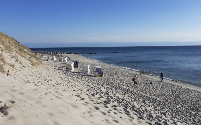Ein Strandpanorama auf der Insel Sylt mit einigen Strandkörben und Personen, sowie Dünen-