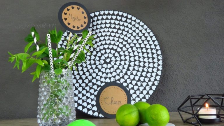 In einem Glas befinden sich Strohhalme und Minzblätter, daneben liegen Limetten und eine brennende Kerze.