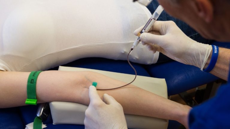Eine medizinische Fachkraft nimmt einem Patienten, von dem nur der Arm zu sehen ist, Blut ab.