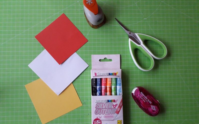 Materialien für den Weihnachtsstern Benötigte Materialien für das Basteln von einem Weihnachtsstern liegen auf einem Tisch, die Materialien sind eine Schere, Klebeband, Stifte und Papier.