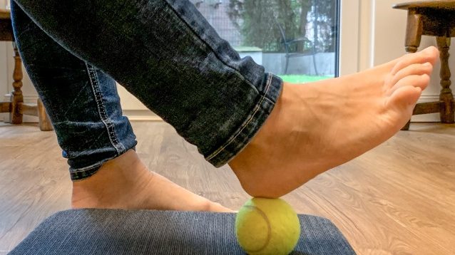 Fuß das einen Tennisball mit der Ferse rollt