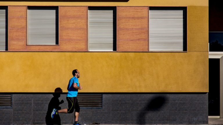 Ein Man mit blauen T-Shirt joggt vor einem Gebäude mit gelber Fassade