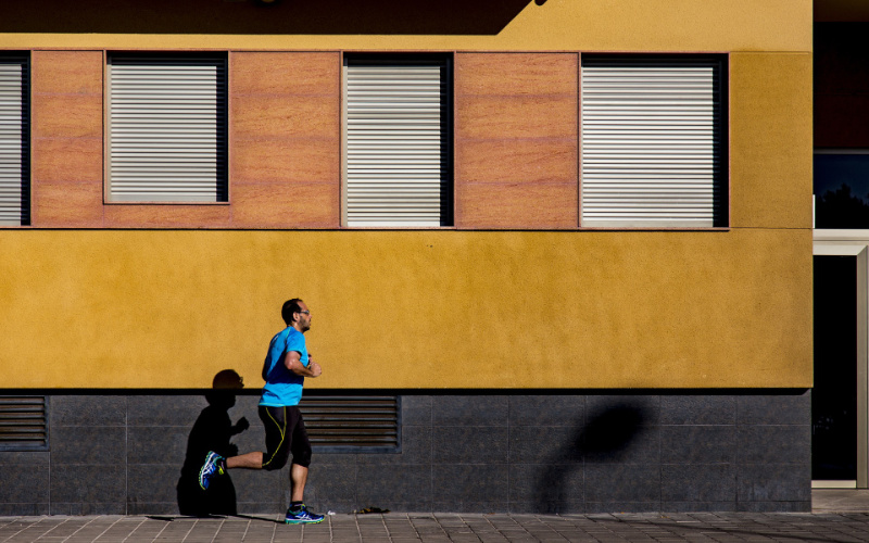Ein Man mit blauen T-Shirt joggt vor einem Gebäude mit gelber Fassade