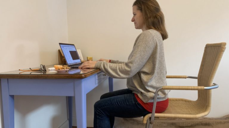 Marei Schachschneider trägt einen grauen Pulli und sitzt auf dem Stuhl vor einem Laptop.