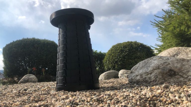 Großaufnahme von Unten von einem Schwarzem Teleskophocker WEDO SITTOGO der im Garten platziert und vom Kies umgeben ist.