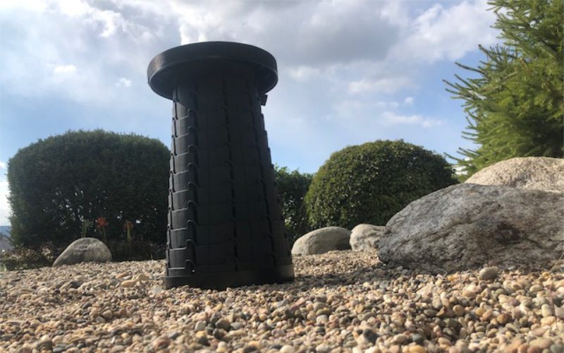 Großaufnahme von Unten von einem Schwarzem Teleskophocker WEDO SITTOGO der im Garten platziert und vom Kies umgeben ist.