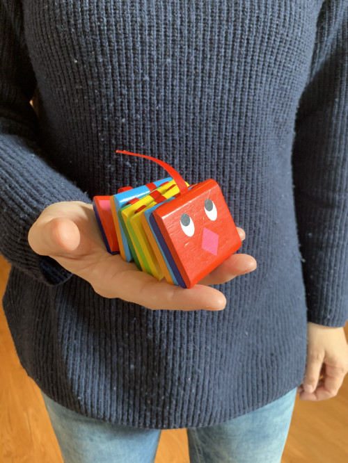 Eine Frau haltet eine bunte viereckige Spielzeugraupe auf ihrer Handfläche.