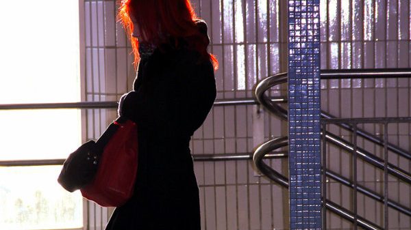 Profil einer rothaarigen Frau in schwarzem Mantel und mit einer roten Tasche in einer U-Bahn Station.