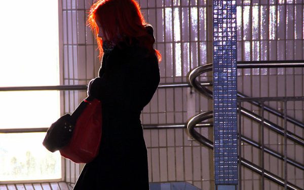 Profil einer rothaarigen Frau in schwarzem Mantel und mit einer roten Tasche in einer U-Bahn Station.
