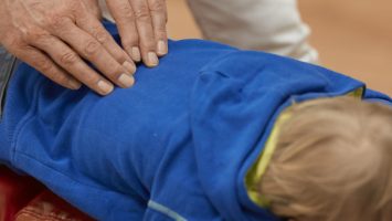 Hände eines Chiroprakters bei der Justierung von einem Kind in blauem Hoody.