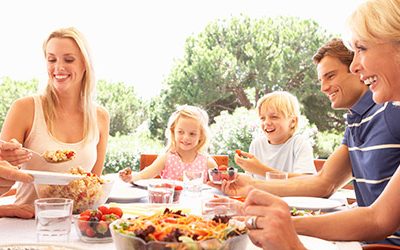 Gesunde-Ernaehrung-mit-der-Familie Eine glückliche Familie sitzt bei einem Mahlzeit am Tisch Draußen.