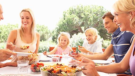 Gesunde-Ernaehrung-mit-der-Familie Eine glückliche Familie sitzt bei einem Mahlzeit am Tisch Draußen.