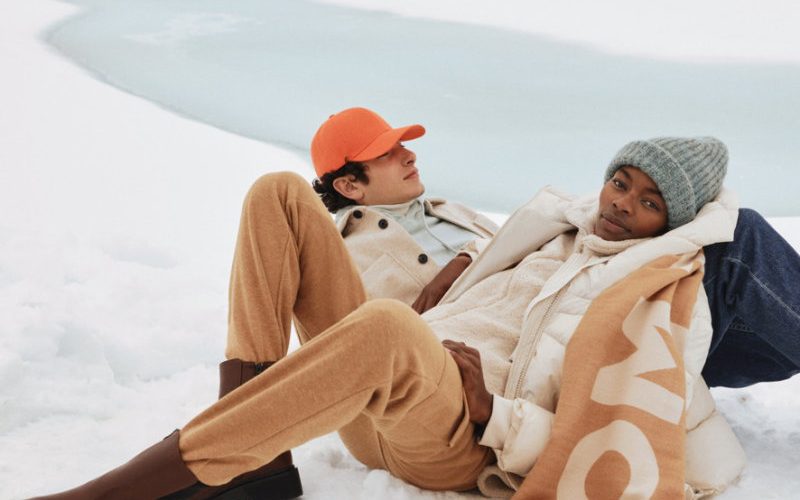 Schnee Ein Man mit orangenen Cappy und eine Frau mit grauer Mütze und Tom Tailor Schall liegen im Schnee.