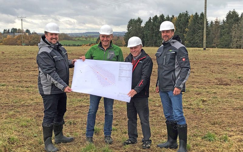 Arbeiter FW Vier Männer mit weissen Helmen halten ein Plan auf einer Wiese.