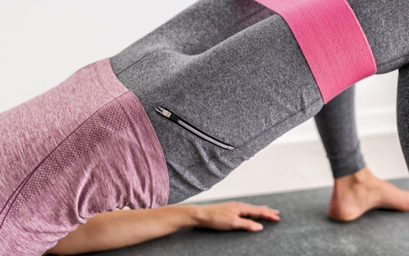 Kraft Eine Frau trainiert auf einer Matte mit pinken Wiederstandsband an ihren Oberschenkel.