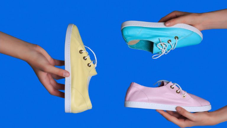 Schuhe Drei Hände halten jeweils drei Turnschuhe in Blau, Pink und Gelb vor einem blauen Hintergrund.