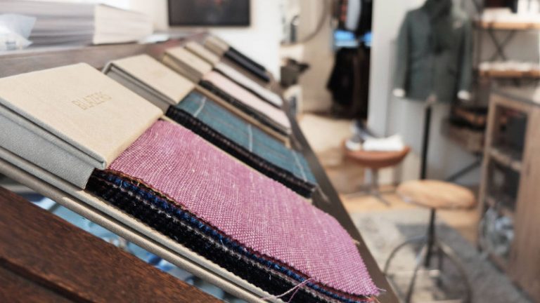 Unterschiedliche Stoffe in einem Schneiderraum liegen an einem Tisch aus Holz.