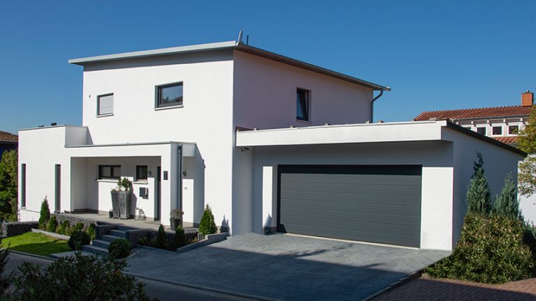 Ein Weisses Haus mit flachen Dach und einer grauen Garage