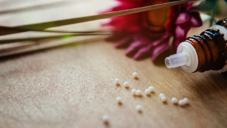 Alternativ-Medizin-2022 Eine Rote Blume und ein Flaschen mit ethärischen Öl liegen auf dem Tisch