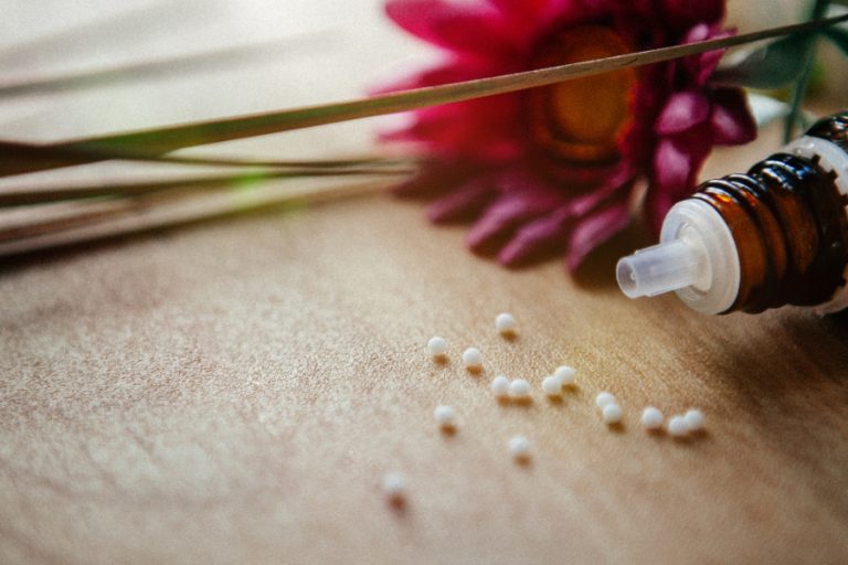 Eine Rote Blume und ein Flaschen mit ethärischen Öl liegen auf dem Tisch