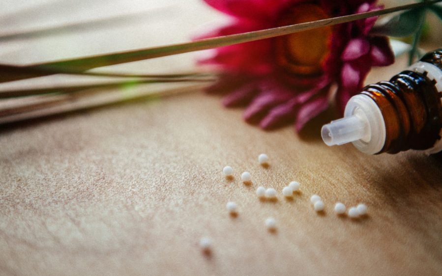 Alternativ-Medizin-2022 Eine Rote Blume und ein Flaschen mit ethärischen Öl liegen auf dem Tisch