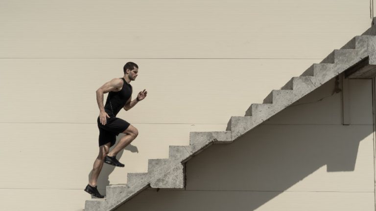 Ein sportlich gekleideter jüngerer Mann, lädt eine Treppe an einer Hauswand hoch.