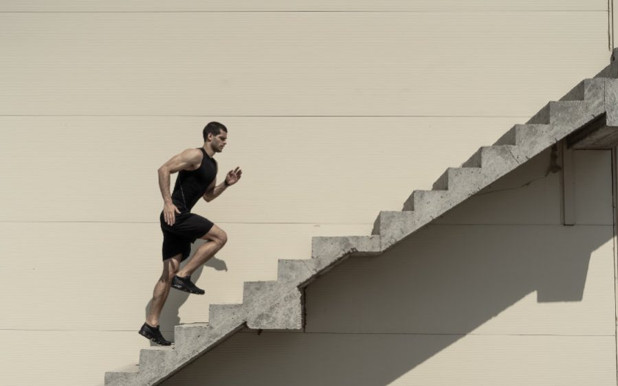 Rennender Mann läuft Treppen hoch Ein sportlich gekleideter jüngerer Mann, lädt eine Treppe an einer Hauswand hoch.