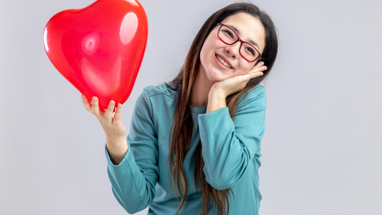 Eine lächelnde Frau hält einen roten Ballon in Form eines Herzes