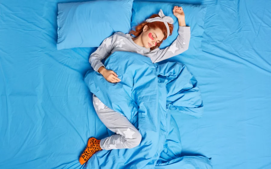 oben-ansicht-der-entspannten-rothaarigen-frau-die-im-pyjama-stirnband-gekleidet-ist-vor-dem-schlafengehen Schlafende junge Frau in einem blauen Bett, die Pyjama und Stirnband trägt