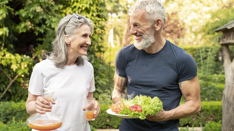 Ein älteres Paar mit Salat und Saft in der Hand, im Garten