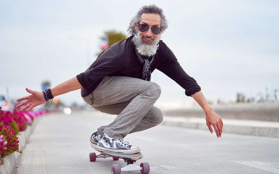 mature man white beard skateboarding on street and having fun Alter Mann der in coolen Klamotten Skateboard fährt